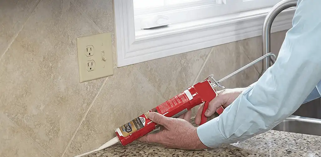 Handyman applying caulk along a kitchen backsplash and countertop seam in Wilmington, NC